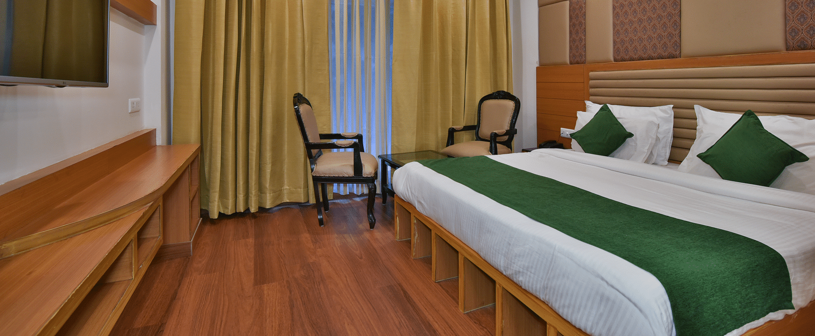 A large bed placed next to two chairs in the Deluxe Room at DLS Highland Resort and Spa, Mussoorie.